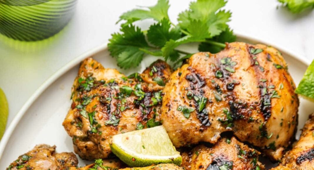 Cooked cilantro lime chicken thighs served on a plate topped with fresh cilantro and lime wedges.