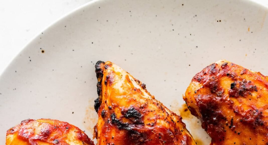 Four grilled BBQ chicken breasts on a white serving plate.