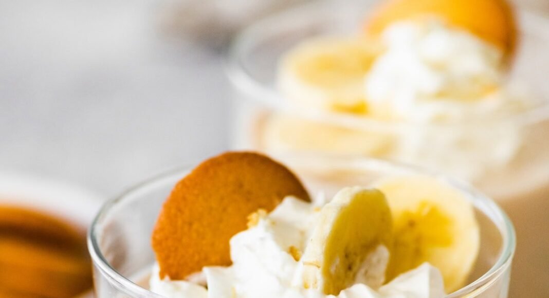 High-protein banana pudding in a glass topped with whipped cream, sliced bananas and a wafer cookie.