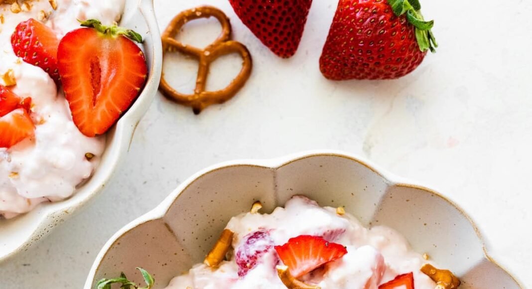 A bowl of strawberry pretzel salad topped with strawberries and crushed pretzels.