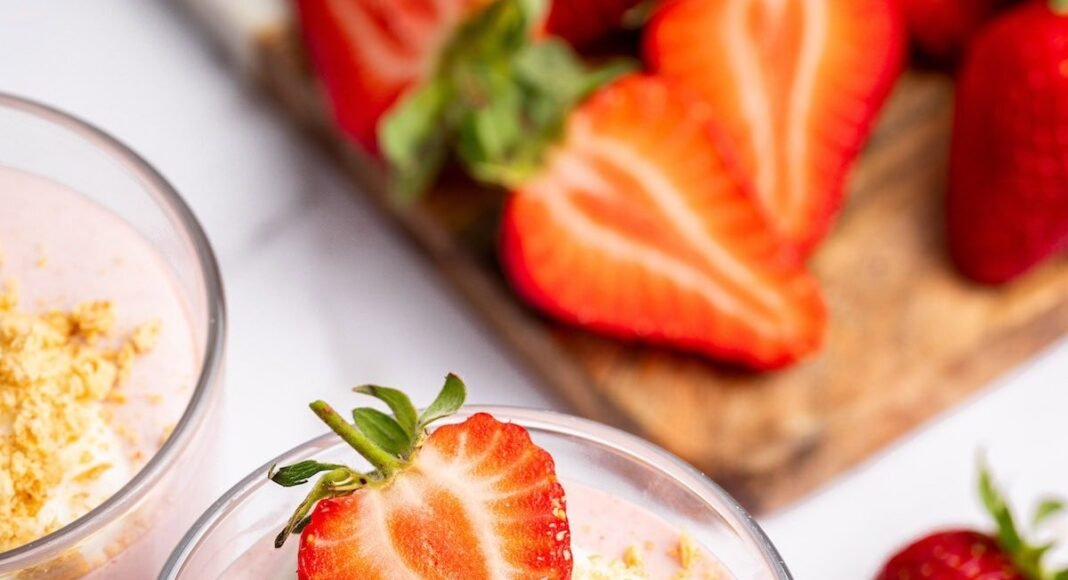 One glass filled with high-protein strawberry mousse topped with a dollop of cocowhip, one halved fresh strawberry and crushed graham crackers.