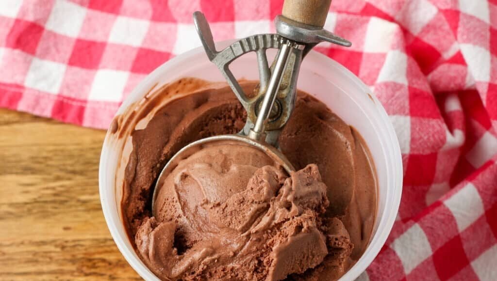 close up horizontal photo of old fashioned ice cream scoop in container of chocolate ice cream