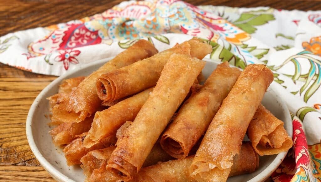 pottery plate stacked with lumpia next to napkin on table