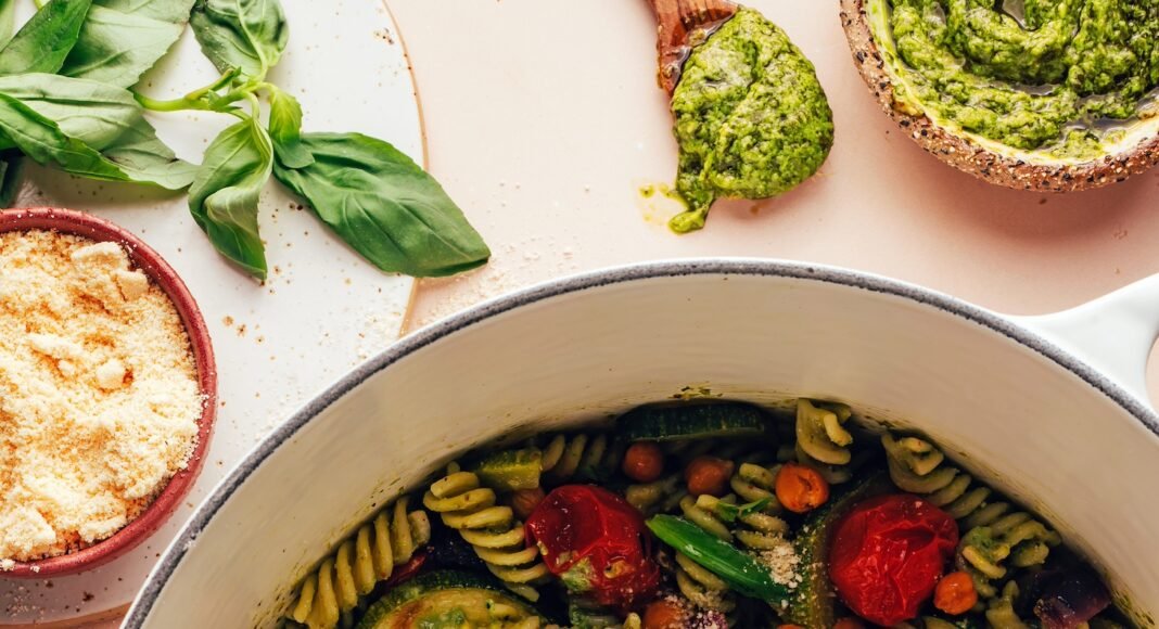 Bowl of vegan parmesan next to a Dutch oven filled with Zucchini Pesto Pasta with Roasted Tomatoes & Chickpeas
