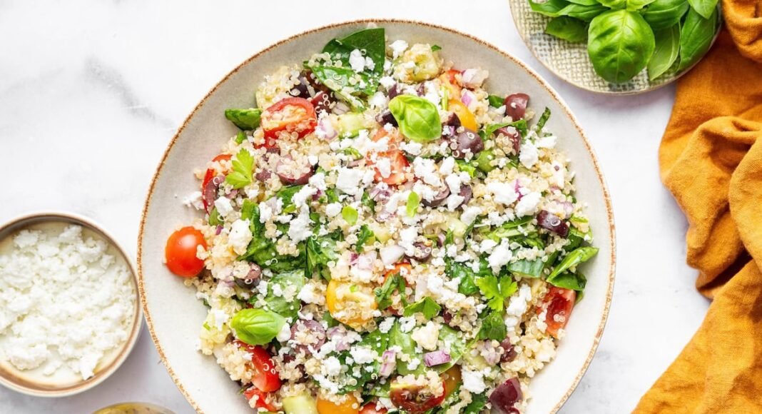 Greek quinoa salad in a tan serving bowl topped with crumbled feta cheese.
