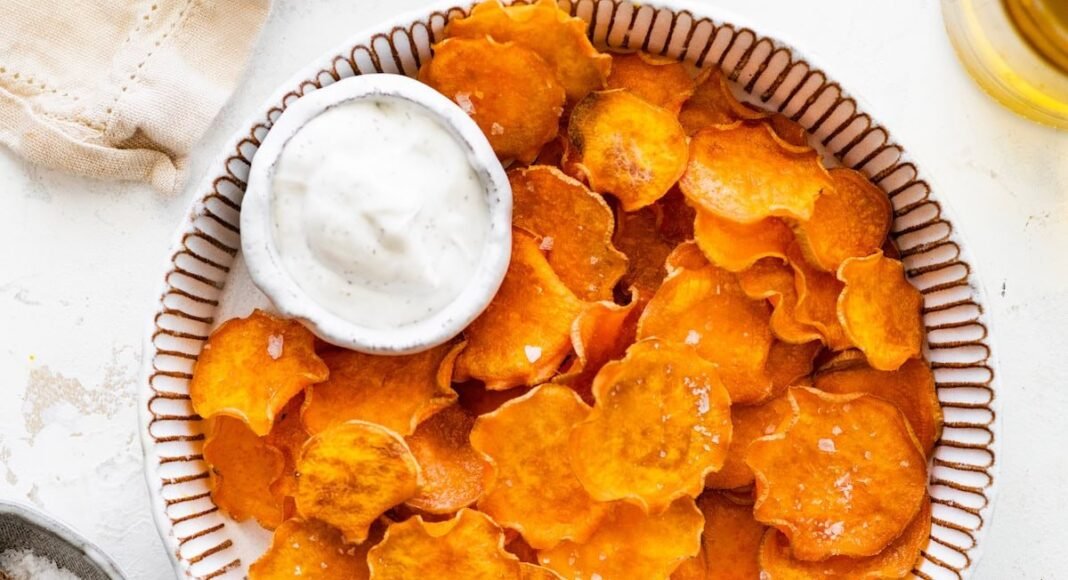 Baked sweet potato chips in a bowl with a small bowl of white dipping sauce.