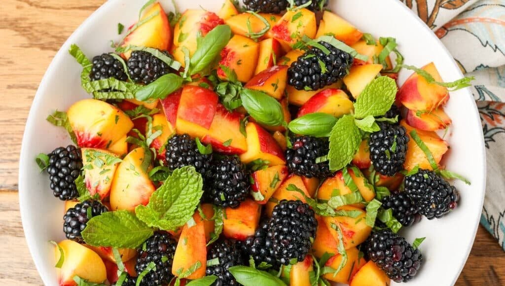 peaches and blackberries and herbs on white plate