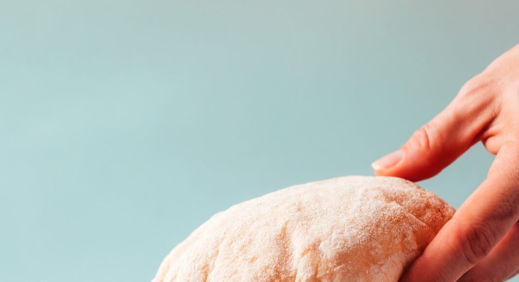 Hand reaching in to pick up a piece of gluten-free pita from a stacked plate of pita