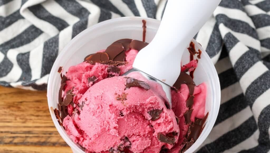 Cranberry-Ice-Cream-BFK-11-1024x731.jpg Cranberry Ice Cream being scooped out of a freezer safe container.