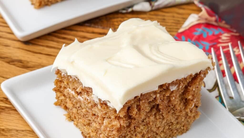 A slice of Crazy Spice Cake sits on a square white plate over a wooden tabletop. 