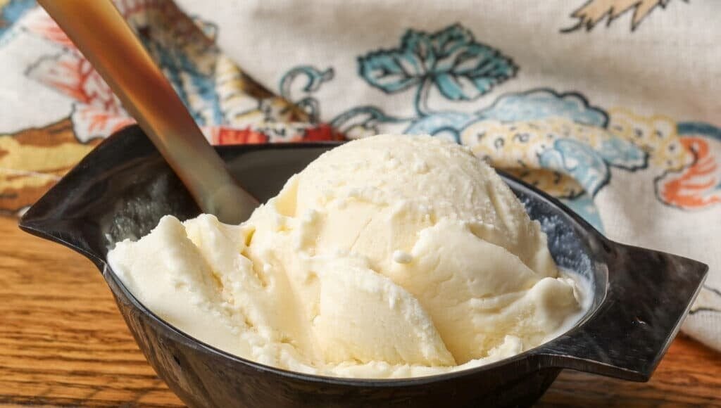 A close up shot of a serving of Mascarpone Ice Cream in a black ceramic bowl on a wooden table. 