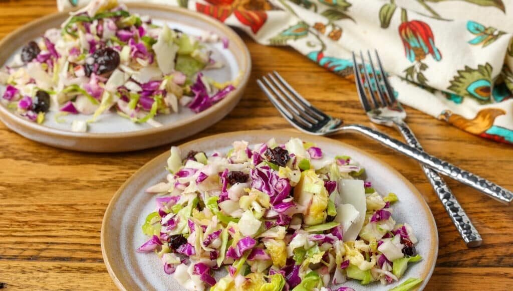 A horizontally aligned image of a ceramic plate piled high with shredded cabbage and sliced Brussels sprouts. 