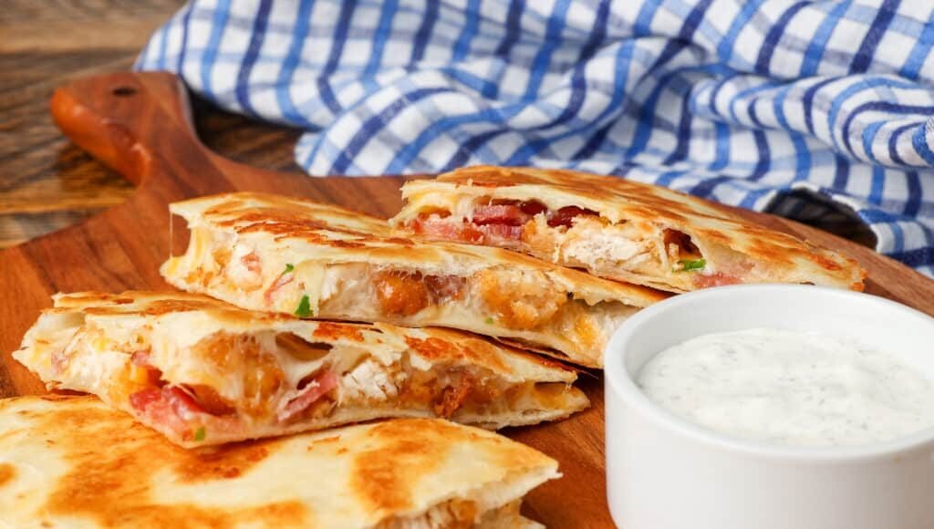 Chicken, bacon, quesadillas on cutting board with a side of ranch dip