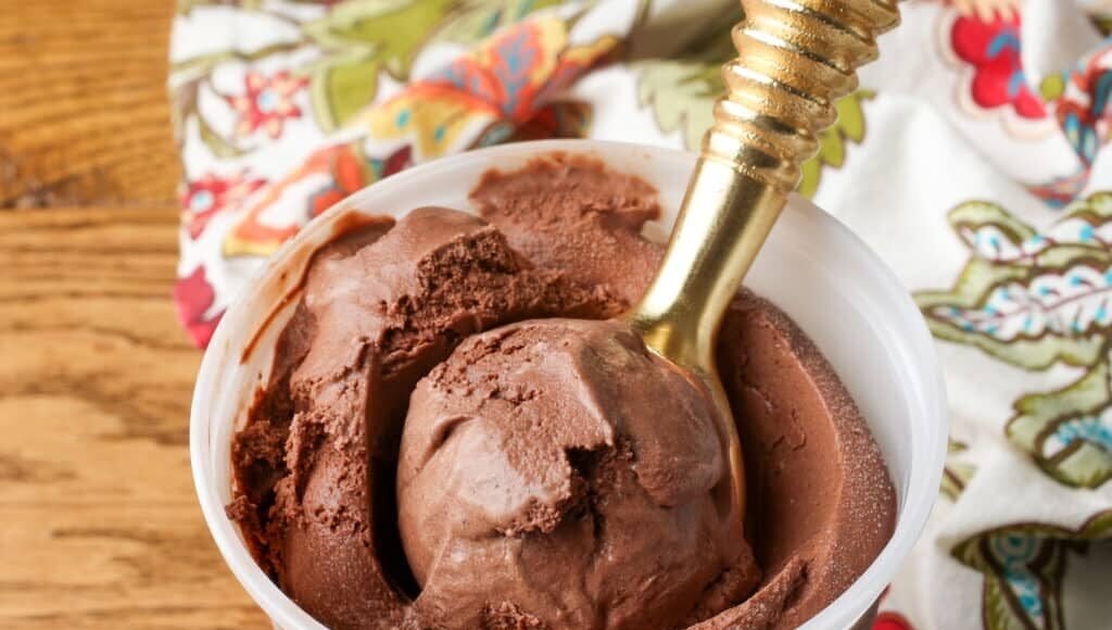 A horizontal photo of a freezer safe container on a wooden tabletop with a floral tea towel visible in the background.