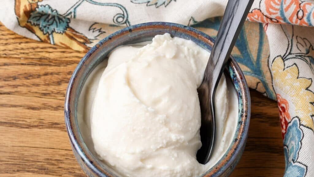 A horizontal close up of luscious white ice cream in a small grey bowl on a wooden tabletop.